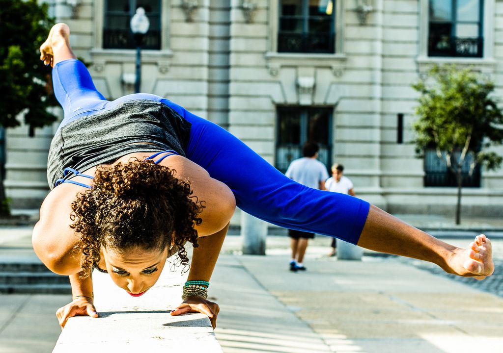 A woman practicing yoga on a ledge in the city incorporating elements of Ar Holistic Therapies.