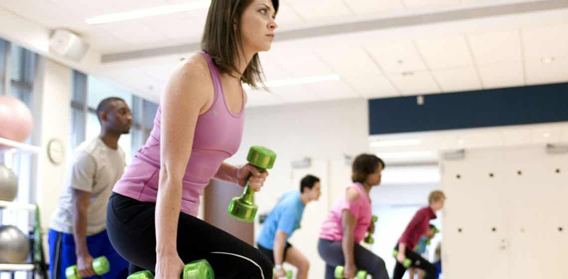 A group of people engaged in dumbbell exercises at a gym, incorporating massage therapy to enhance their workout.