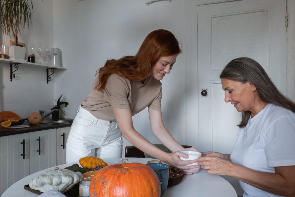 A woman is aiding an older woman with a pumpkin, promoting relaxation therapy and mind-body harmony through their interaction.