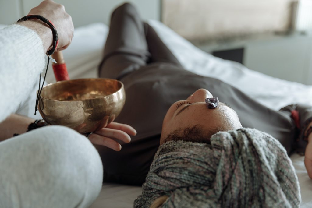 Ar Holistic Therapy - Bradford - A woman experiencing the power of touch as she rests on a bed with a singing bowl balancing delicately atop her head.