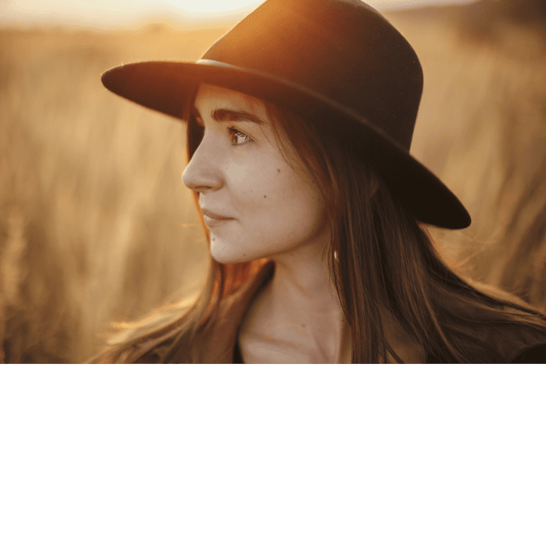 Ar Holistic Therapy - Bradford - A woman wearing a hat in a field at sunset, exuding an aura of tranquility and neutrality.
