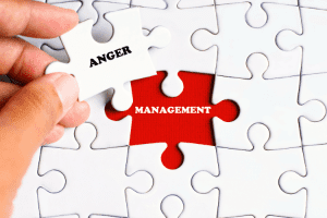 Ar Holistic Therapy - Bradford - Hand placing the final puzzle piece with the word "anger" into a jigsaw puzzle with a red piece that has the word "management" printed on it.