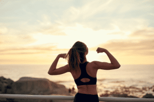 Ar Holistic Therapy - Bradford - Woman flexing muscles while facing a sunset over the ocean.