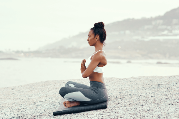 Ar Holistic Therapy - Bradford - A woman is peacefully meditating on a rock overlooking the vast expanse of the ocean, practicing conscious living.